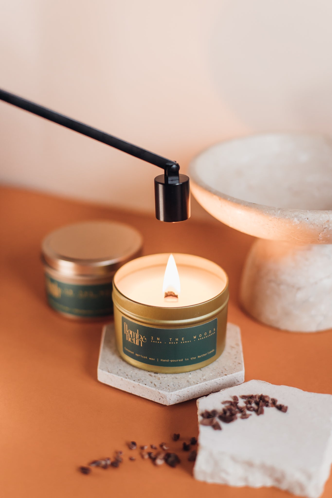 Non Toxic, vegan Candle in a gold tin with a green label on a wooden surface, surrounded by small containers and a lamp. Wooden wick