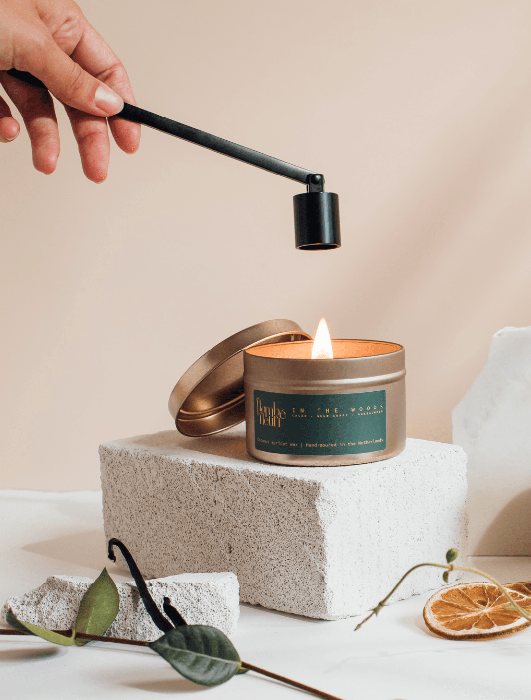 Hand lighting a vegan, non toxic candle in a gold metal tin with a decorative label on a neutral background. Wooden wick 